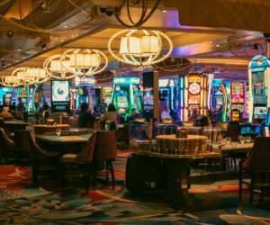 Uma sala de jogos de um cassino físico com pessoas, mesas e máquinas caça-níqueis.
